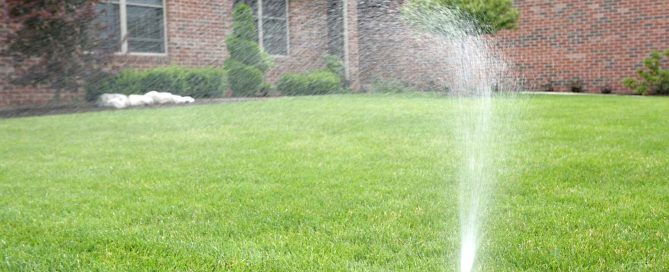 A residential lawn sprinkler spraying water in the front lawn of a house.